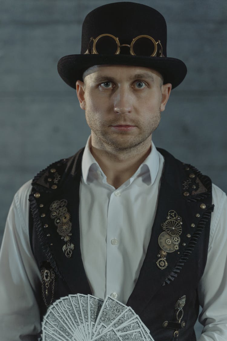 Man In White Shirt Wearing Black Hat And Black Vest Holding Fan Of Cards