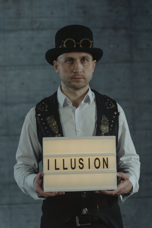 Free A steampunk magician holding a sign spelling 'ILLUSION', set against a dark background indoors. Stock Photo