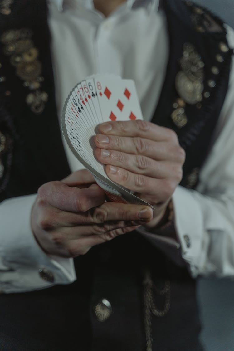 Person In Black Vest Holding Fan Of Cards