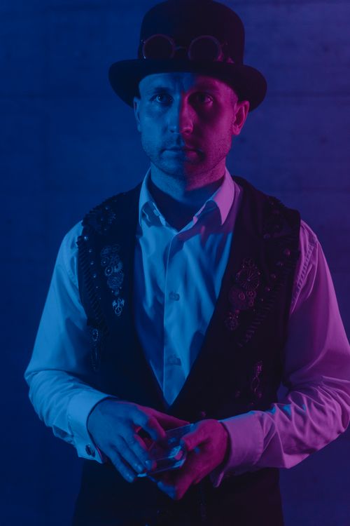 Free Magician in a black hat performing a card trick under dramatic blue and purple lighting. Stock Photo