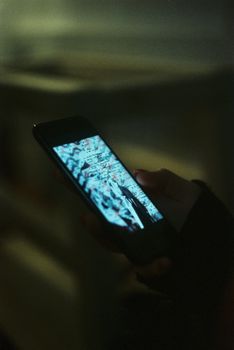 A person holding a smartphone, screen lit up, in a dark indoor setting.