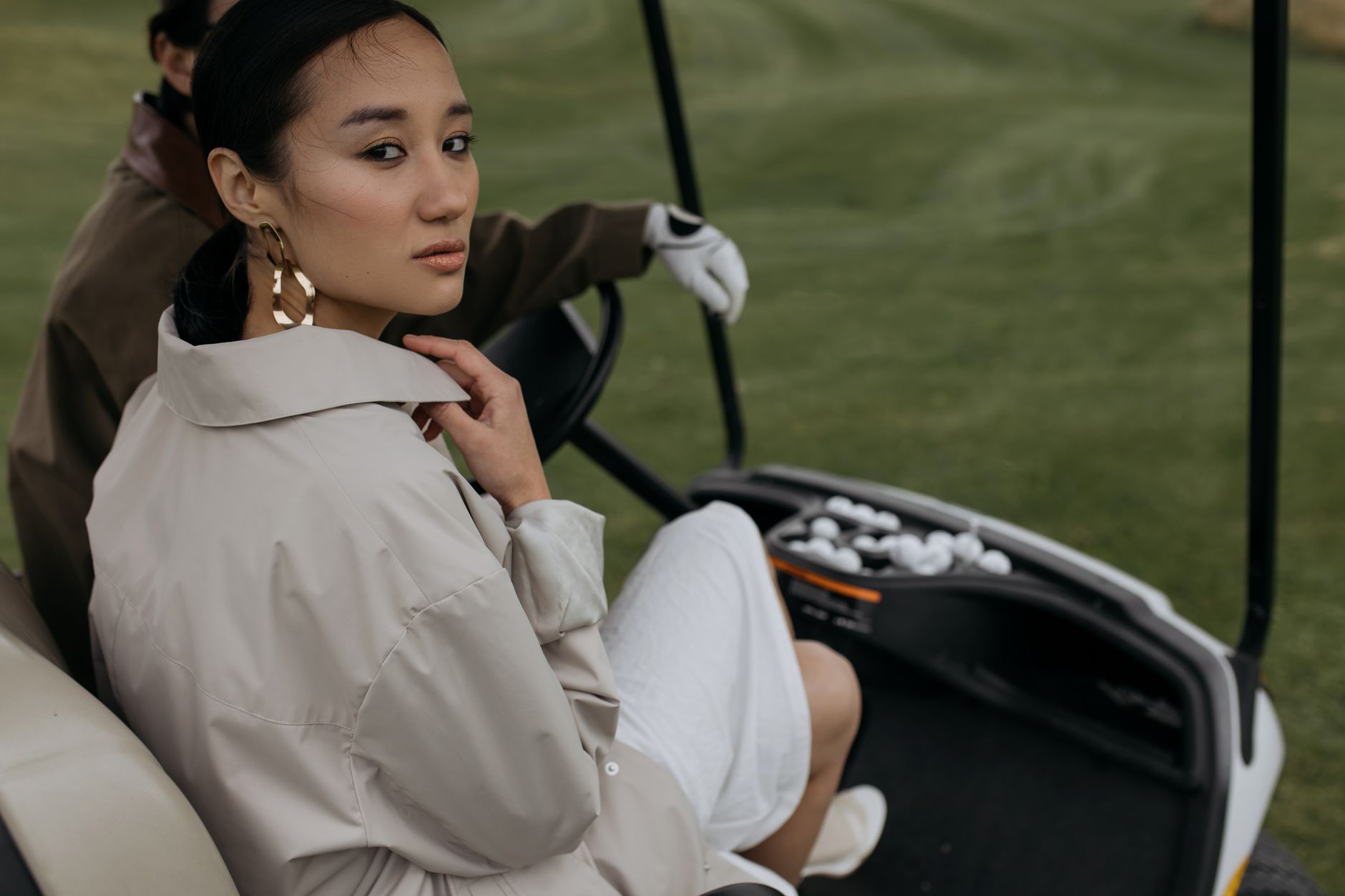 A stylish Asian woman sitting in a golf cart on a lush green golf course. Elegant and sophisticated atmosphere.