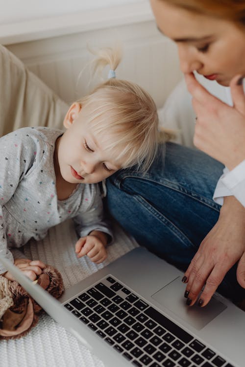 Free Mother Using Laptop with her Child Sitting Nearby  Stock Photo