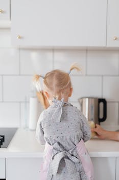 Back view of a girl in a gray apron cooking in a modern white kitchen.