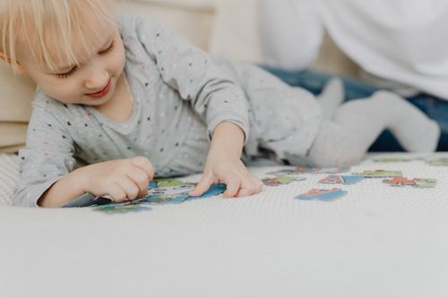 Free Smiling toddler playing with colorful puzzles on a bed indoors. Stock Photo