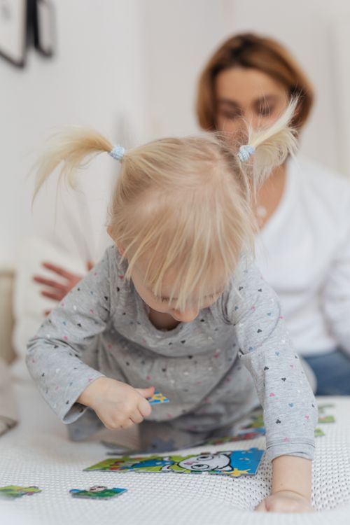 Free A blonde child and mother enjoying puzzle time indoors. Perfect for family and education themes. Stock Photo