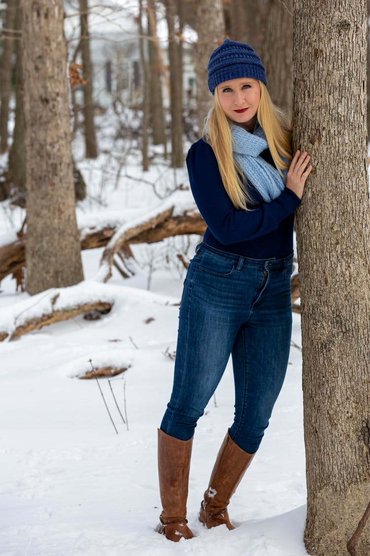 Smiling Woman In Hat Leaning On Tree In Winter Woods