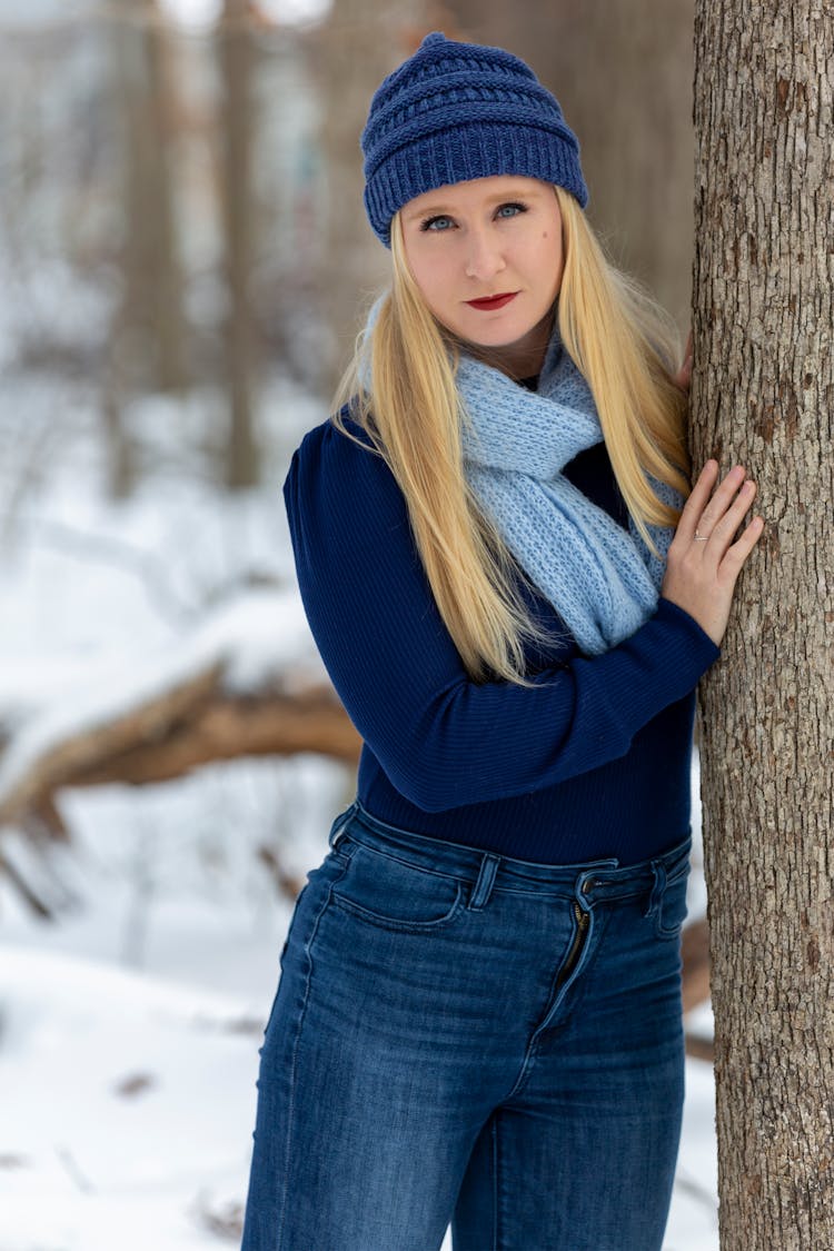 Serious Woman In Hat Leaning On Tree In Winter Nature