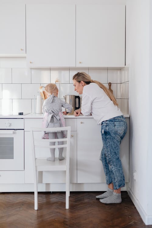 Free Mother and Daughter Standing on a Chair Preparing Food in the Kitchen  Stock Photo