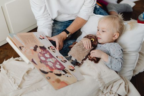 Free A young child reading a storybook with a parent, cuddling a toy owl. Stock Photo