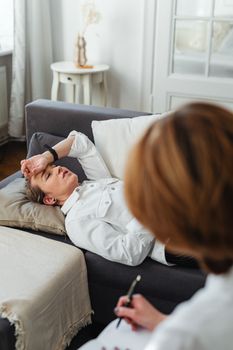 Woman in therapy session relaxing on sofa, attended by therapist in a professional setting.