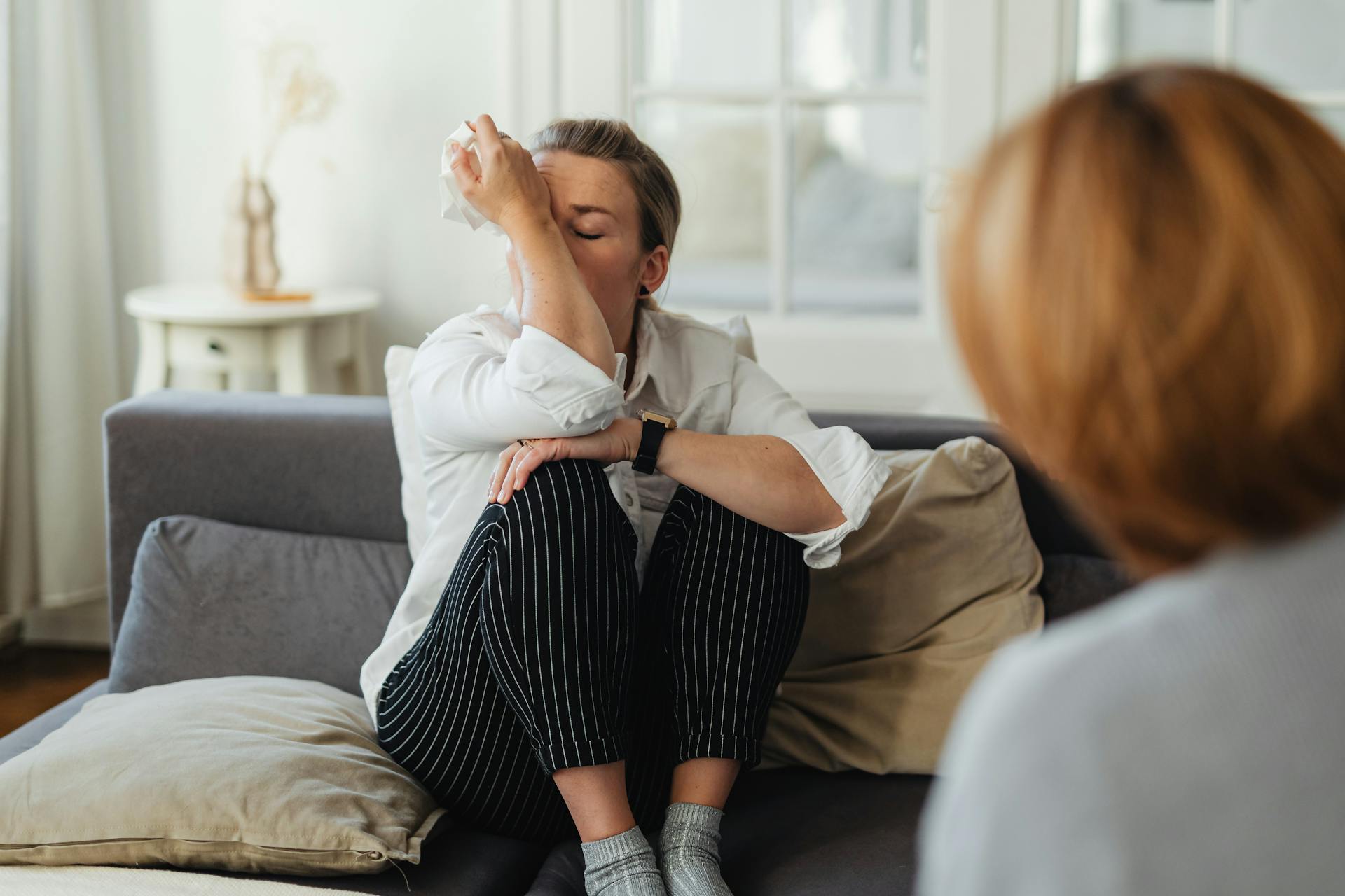 A woman wipes tears during a therapy session on a couch indoors.