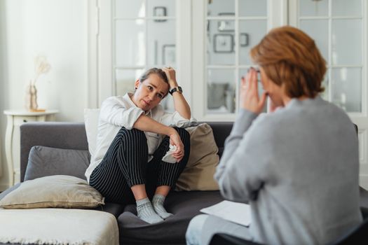 A woman sits on a couch during a therapy session, talking to a therapist.
