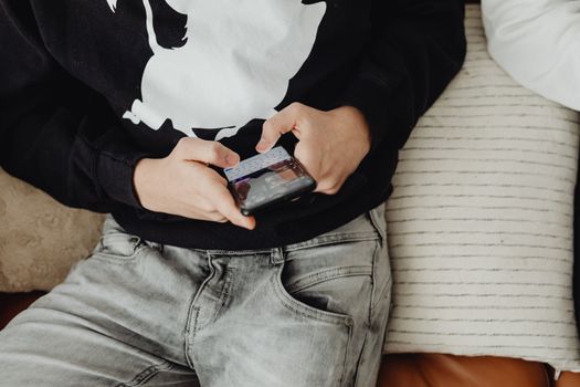 Close-up of a teenager sitting and using a smartphone on a comfortable sofa.