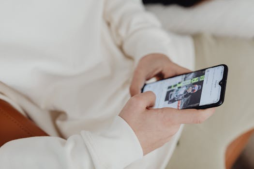 A close-up view of hands holding a smartphone displaying a sports image indoors.