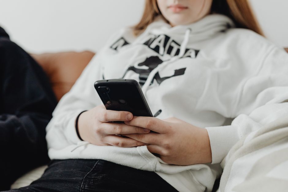 A teenage girl in a white hoodie using a smartphone, focusing on connection and technology.