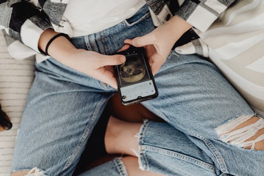 Person using smartphone while wearing casual ripped jeans indoors.