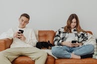 Young Man and Woman Sitting on Sofa Beside a Dog while Using Cellphones