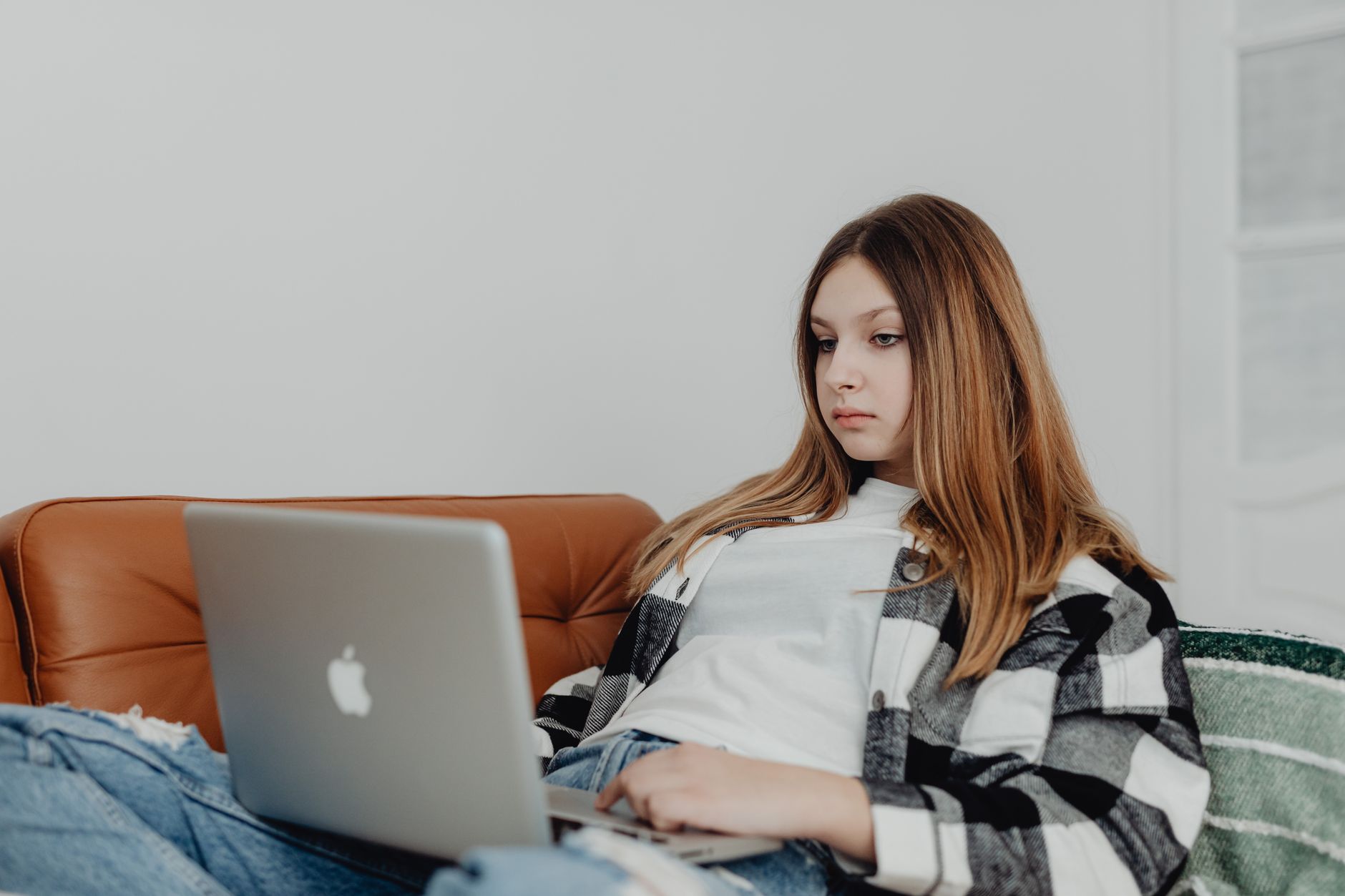 Młoda kobieta siedząca na kanapie, korzystająca z laptopa położonego na kolanach