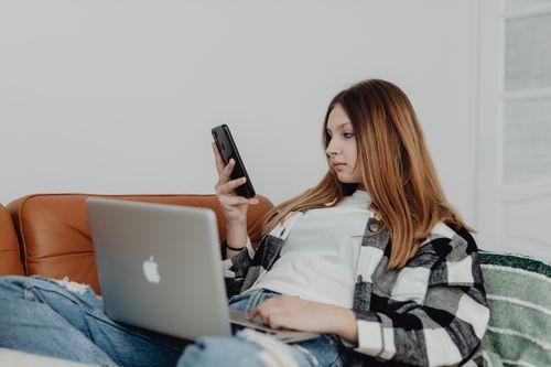 Free Teen girl enjoying leisure time on a sofa with smartphone and laptop indoors. Stock Photo
