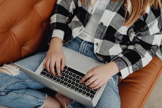 Young woman typing on a laptop while sitting comfortably on a sofa, wearing casual clothes.
