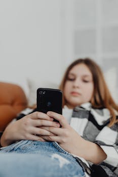 Teen lying on a couch using a smartphone for leisure. Indoors lifestyle scene.