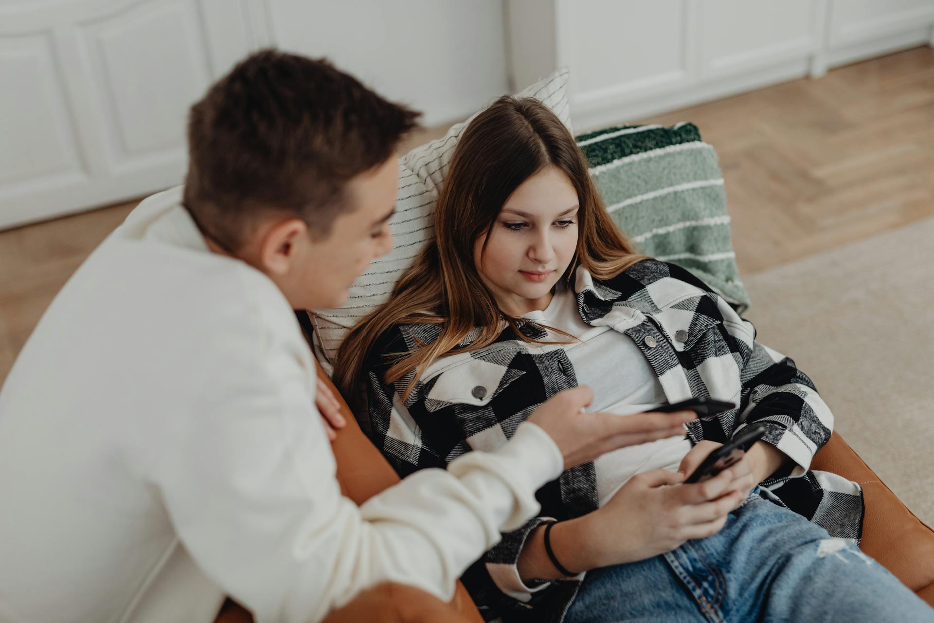 Young couple relaxing on sofa using smartphones in a cozy room setting.