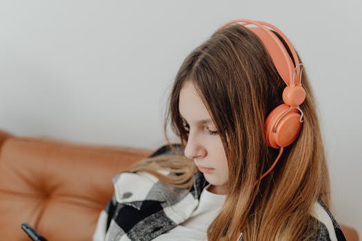 A young woman with brown hair wearing orange headphones, deeply engaged in listening to music.