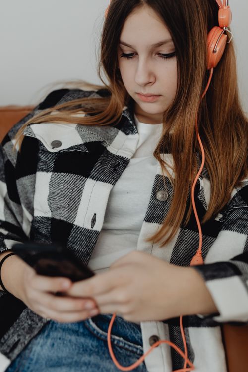 Free Teen girl with headphones using smartphone indoors, focused and relaxed. Stock Photo