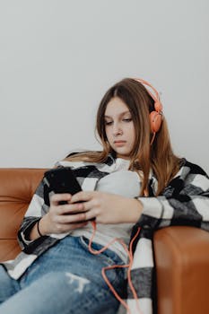 Teenager in headphones relaxing on a sofa, listening to music using a smartphone.