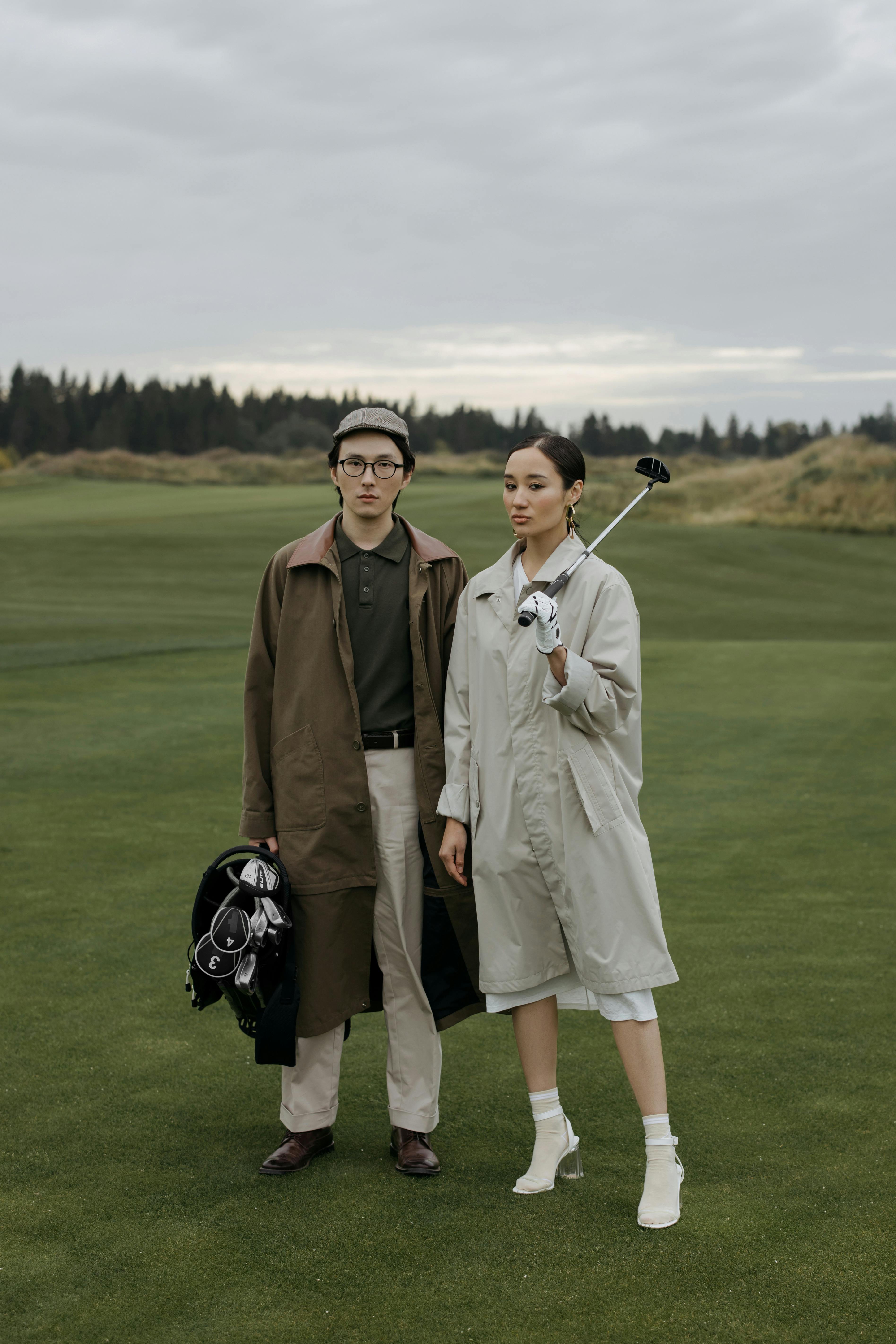 Fashionable couple with golf accessories standing on a course on a cloudy day.