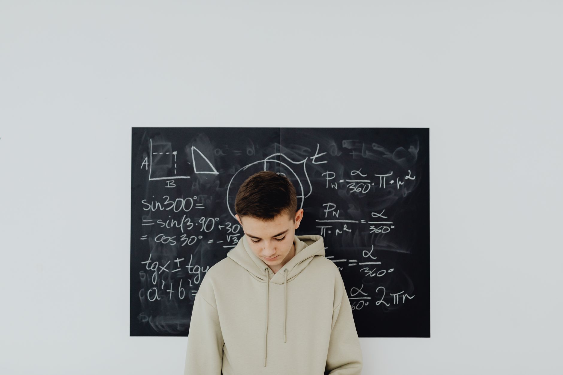 Teenager in a classroom solving mathematics equations on a blackboard, deep in thought.