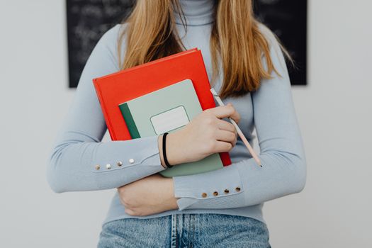 Close-up of a student holding colorful notebooks and a pencil in a classroom setting.