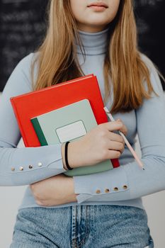 Teenage girl holding textbooks and a pen in a classroom setting, embodying education.