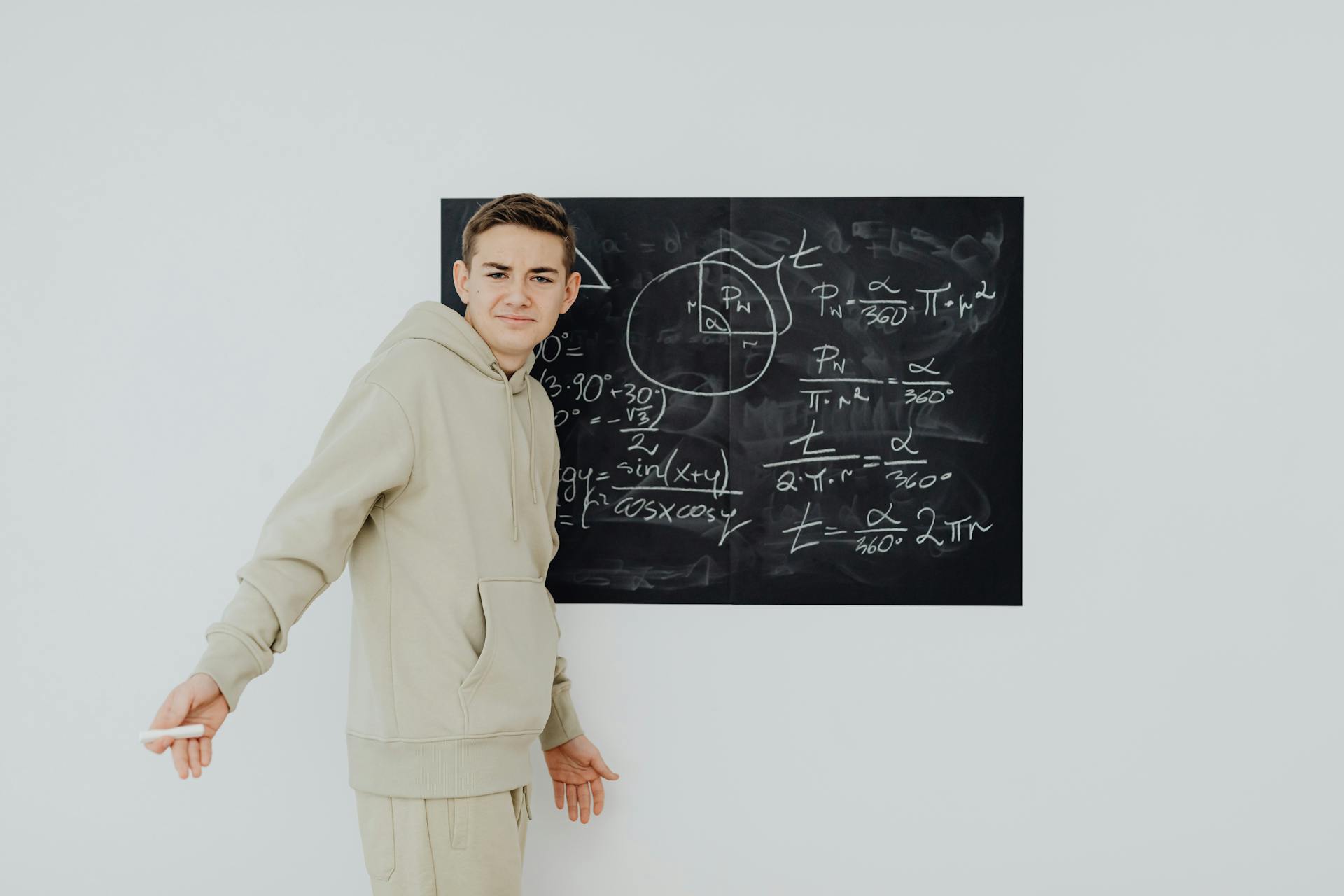 Teenager in casual clothes solving math equations on a blackboard indoors.