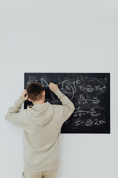 Free Boy Trying to Solve a Mathematical Equation in front of a Blackboard Stock Photo