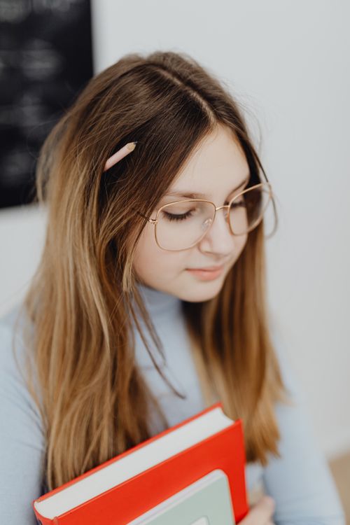 Free A student wearing eyeglasses holding books against a classroom backdrop. Stock Photo