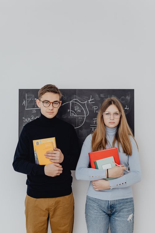 Free Two students hold books with a blackboard background, reflecting a classroom setting. Stock Photo