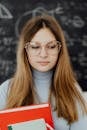 Girl Holding Books and Standing in front of a Blackboard