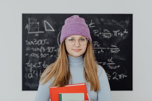 Teenage girl wearing glasses and a beanie, studying math indoors with a blackboard background.