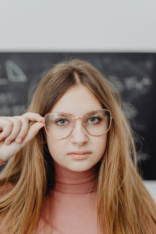 Free Stylish woman wearing eyeglasses poses confidently in a soft indoor setting. Stock Photo