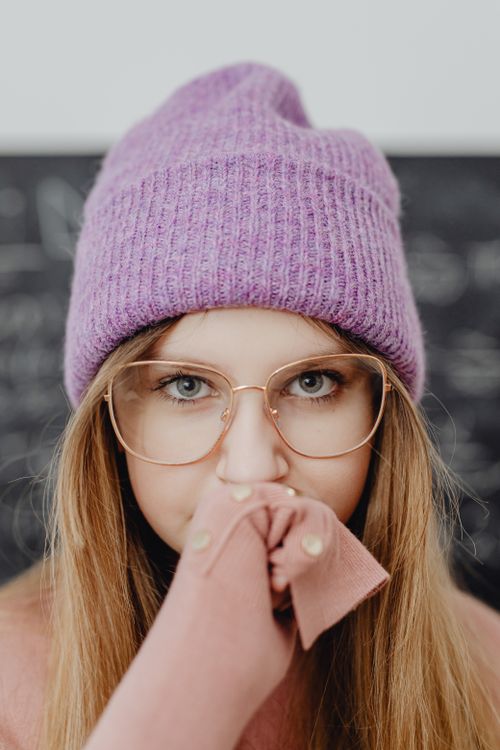 Free Young woman with long hair wearing a pink beanie and glasses. Close-up portrait. Stock Photo