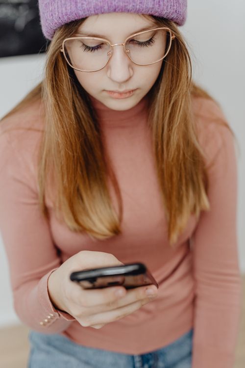 Free A young woman with glasses focuses on her smartphone indoors Stock Photo