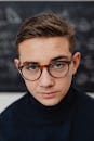 Portrait of a Young Man in Eyeglasses with a Blackboard Behind Him