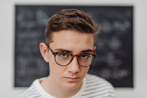 Free Portrait of a Young Man in Eyeglasses in front of a Blackboard  Stock Photo