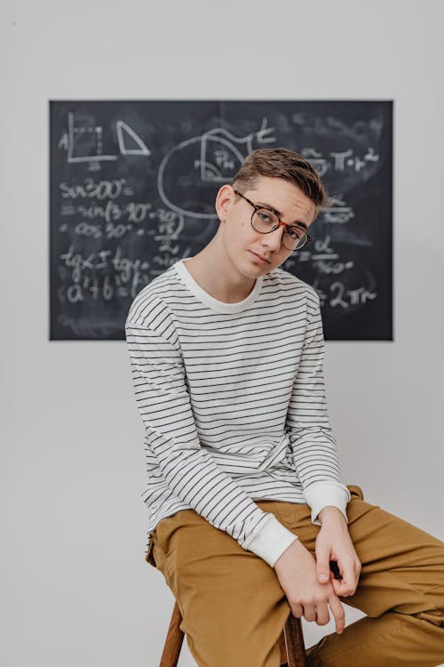 Teenage Boy Sitting in front of a Blackboard 