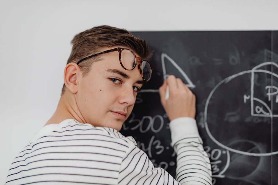 Teen boy writing math equations on a blackboard in a classroom setting. Teen boy writing math equations on a blackboard in a classroom setting.