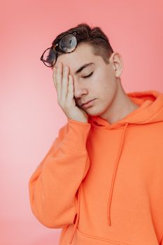 Portrait of a young man with glasses resting on his head, wearing an orange hoodie against a soft pink background. - Fotografer Sidoarjo