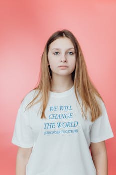 Young woman wearing a motivational text t-shirt, posing against a pink background.