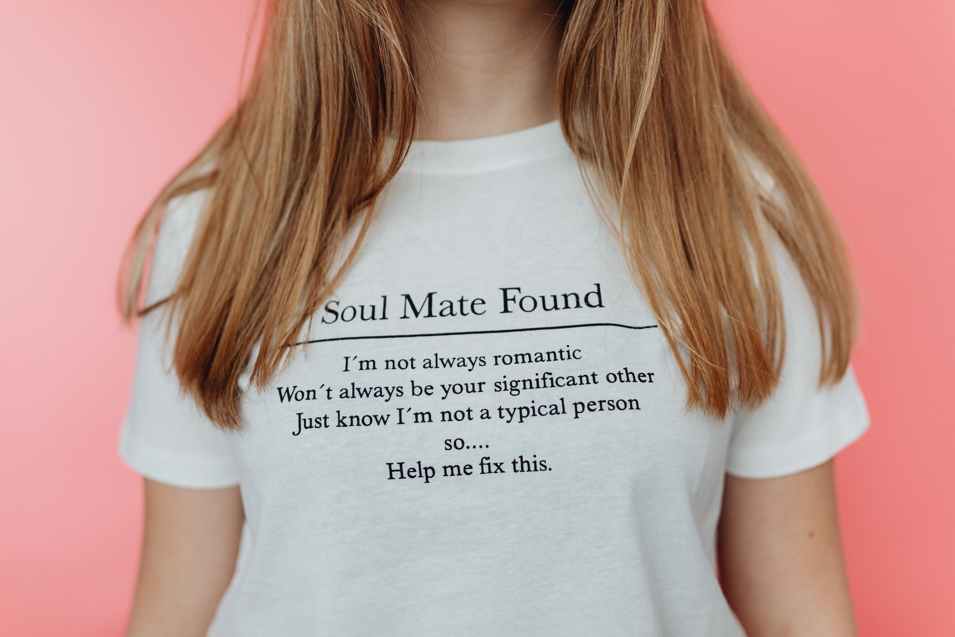 Close-up of a woman in a white t-shirt with quirky text against a pink background.